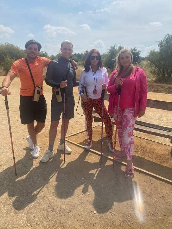 Four people standing outdoors on a sunny day, holding trekking poles.
