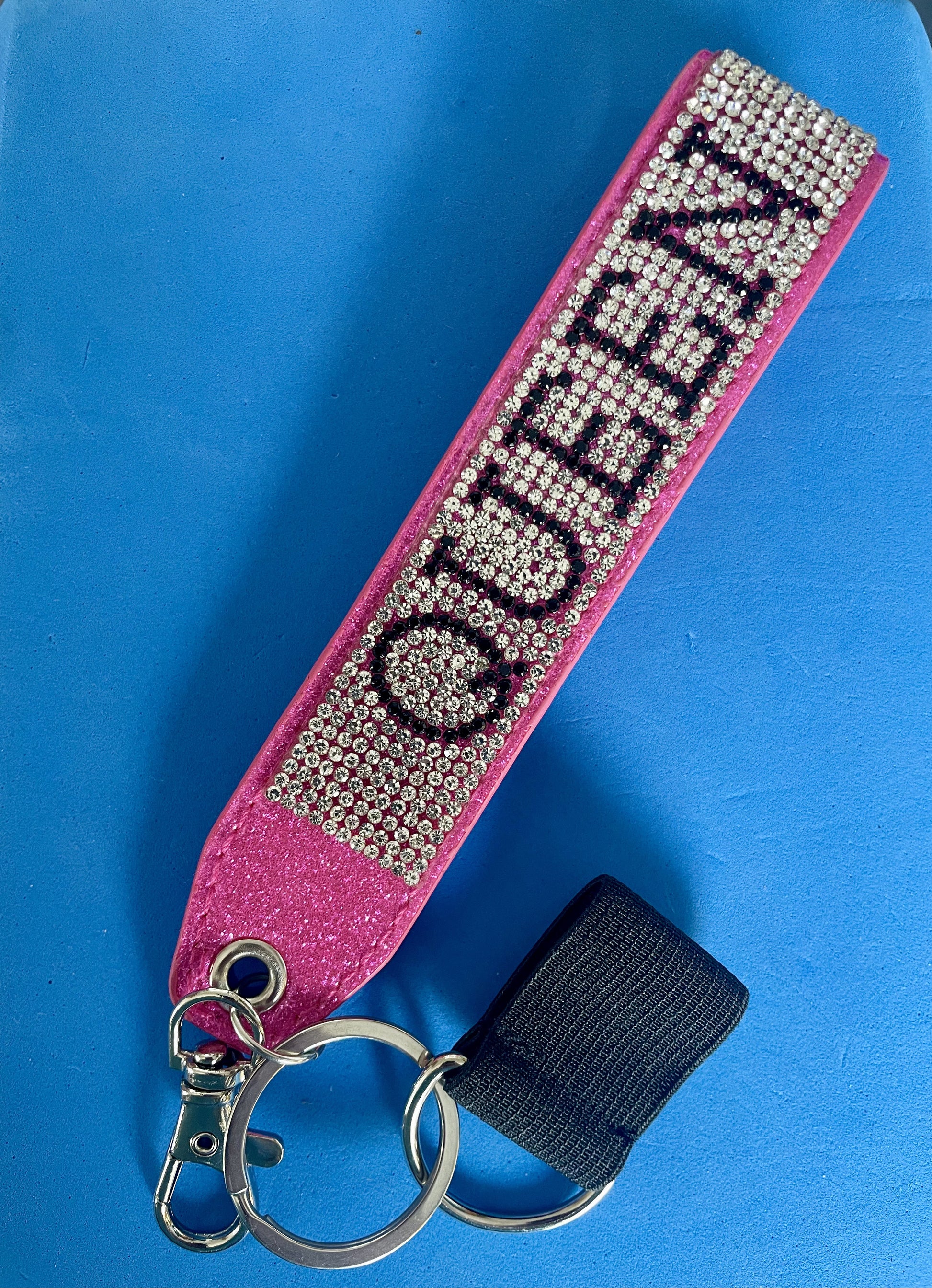 On a pink strap sits silver sparkles with the word QUEEN in black sparkles