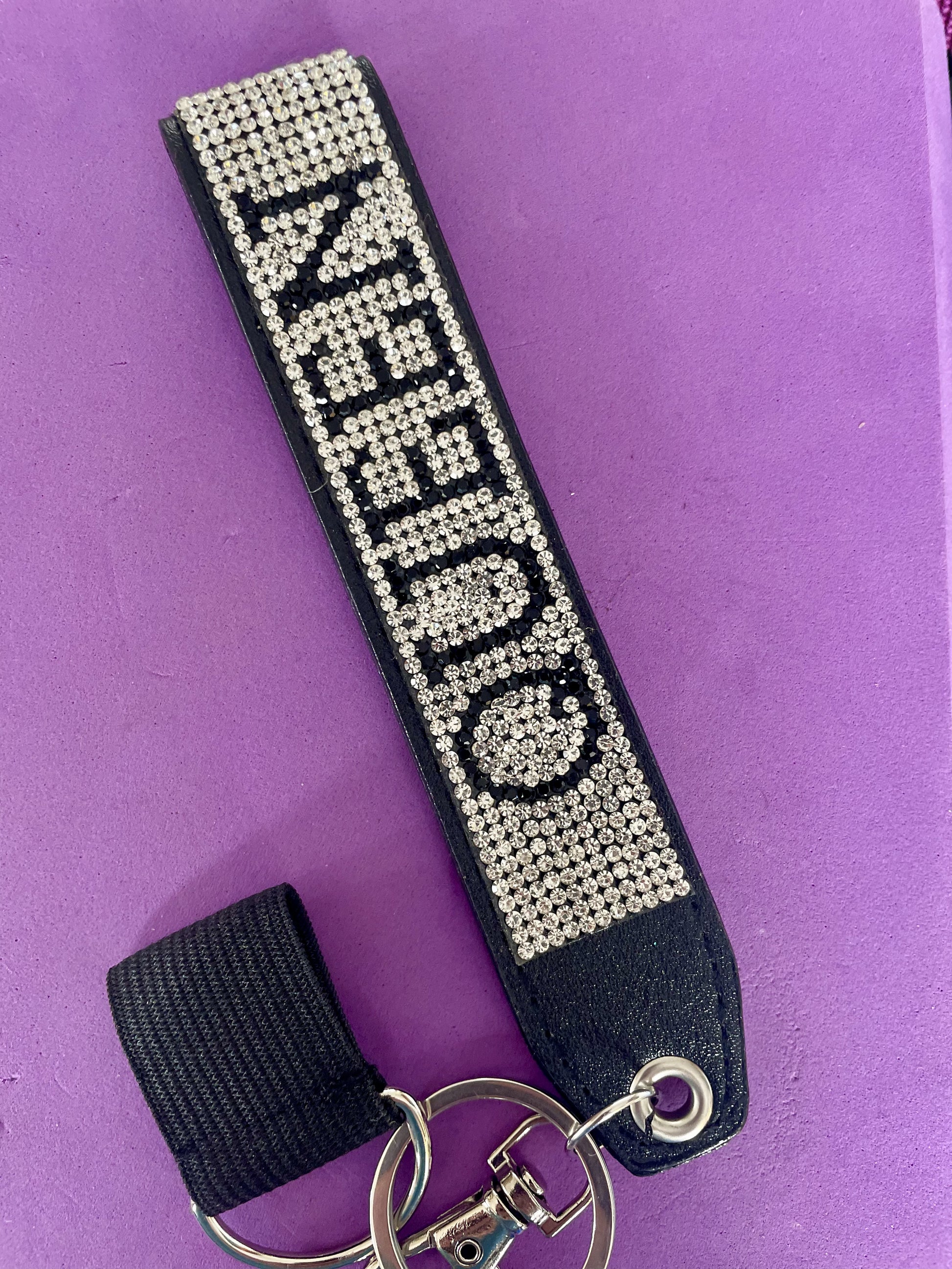 On a black strap sits silver sparkles with the word QUEEN in black sparkles