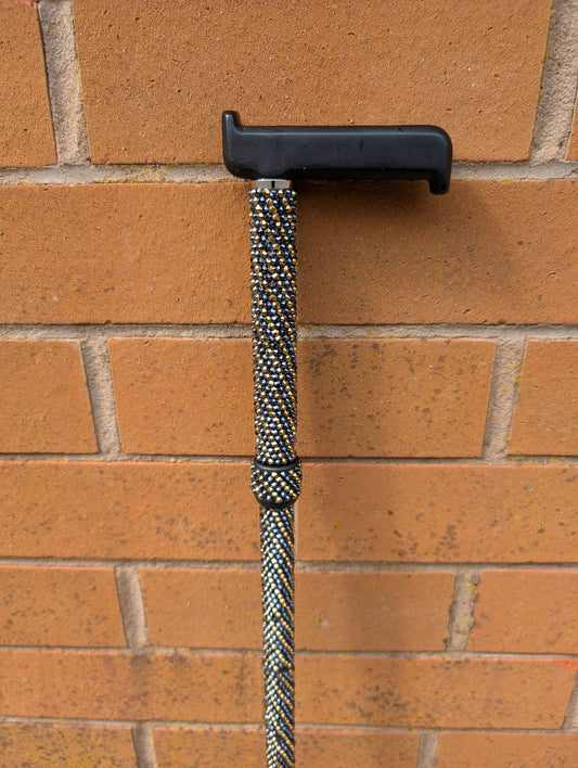 black and gold walking stick with black handle against a brick wall