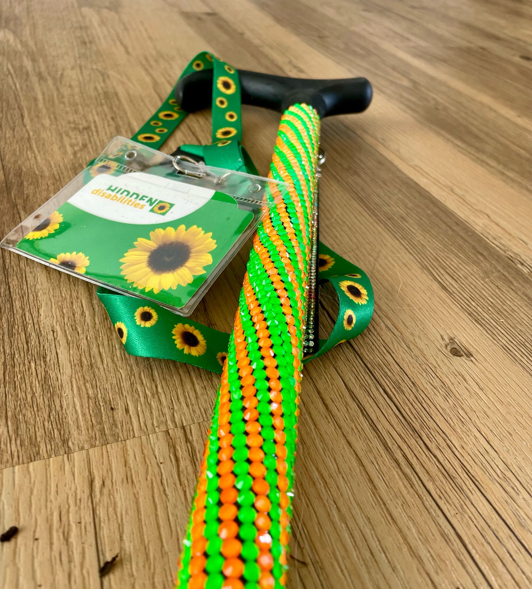Helenix green and orange walking stick with black handle and sunflower lanyard on a wooden floor
