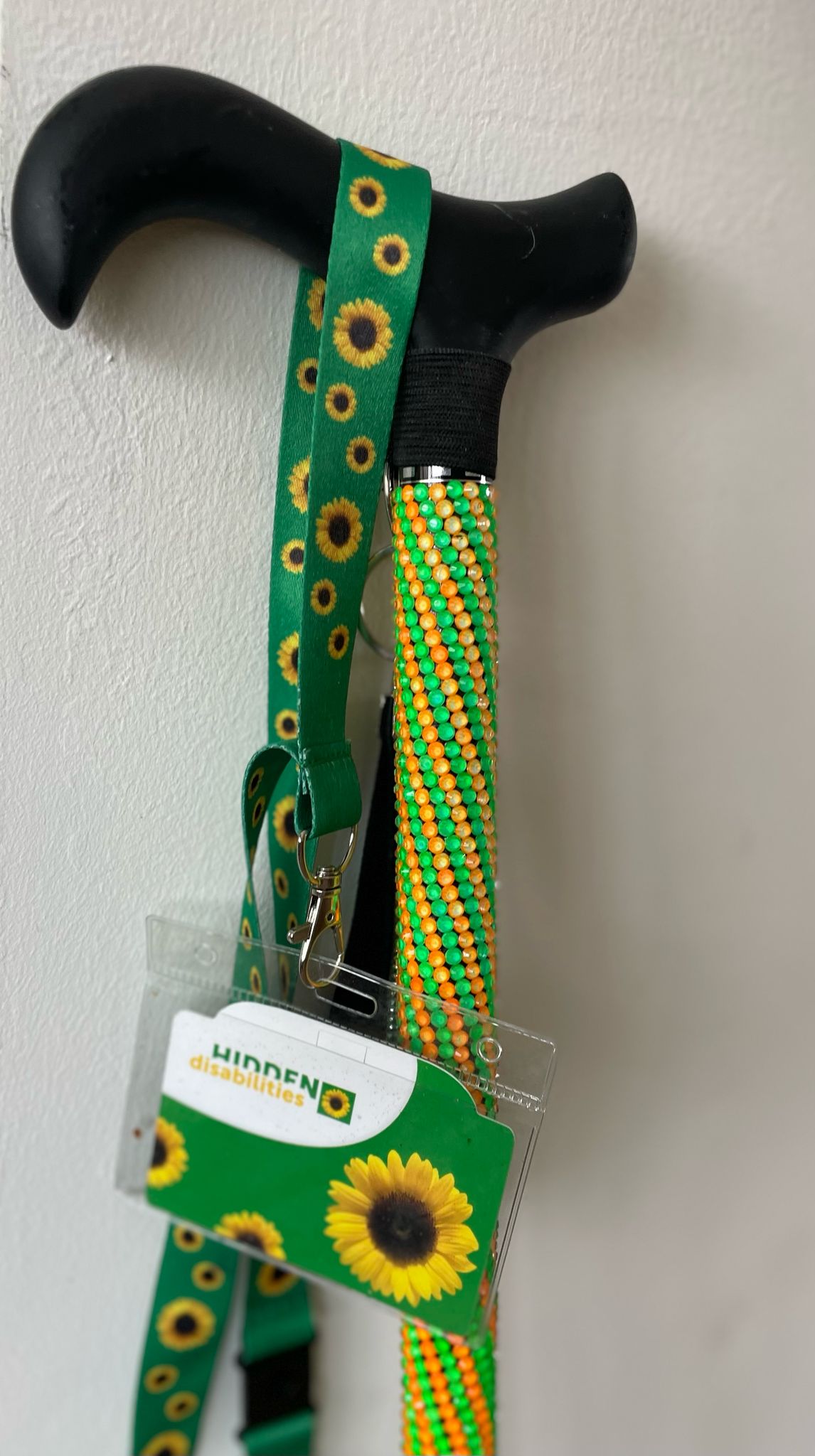 green and orange stick walking stick with black handle and hanging sunflower lanyard