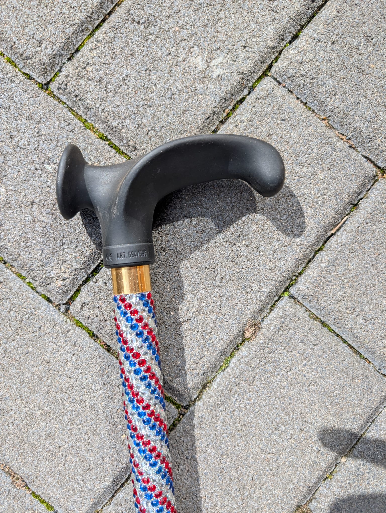 Cane handle with black grip and red, white, and blue Rhinestones on a stone pavement