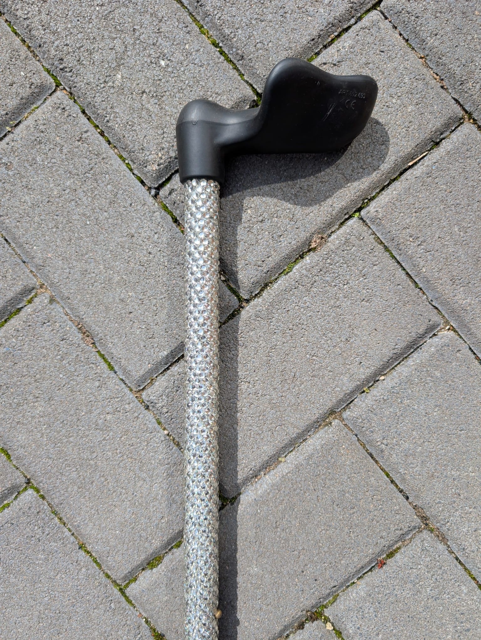 Crstal walking stick with a black handle on a grey pavement