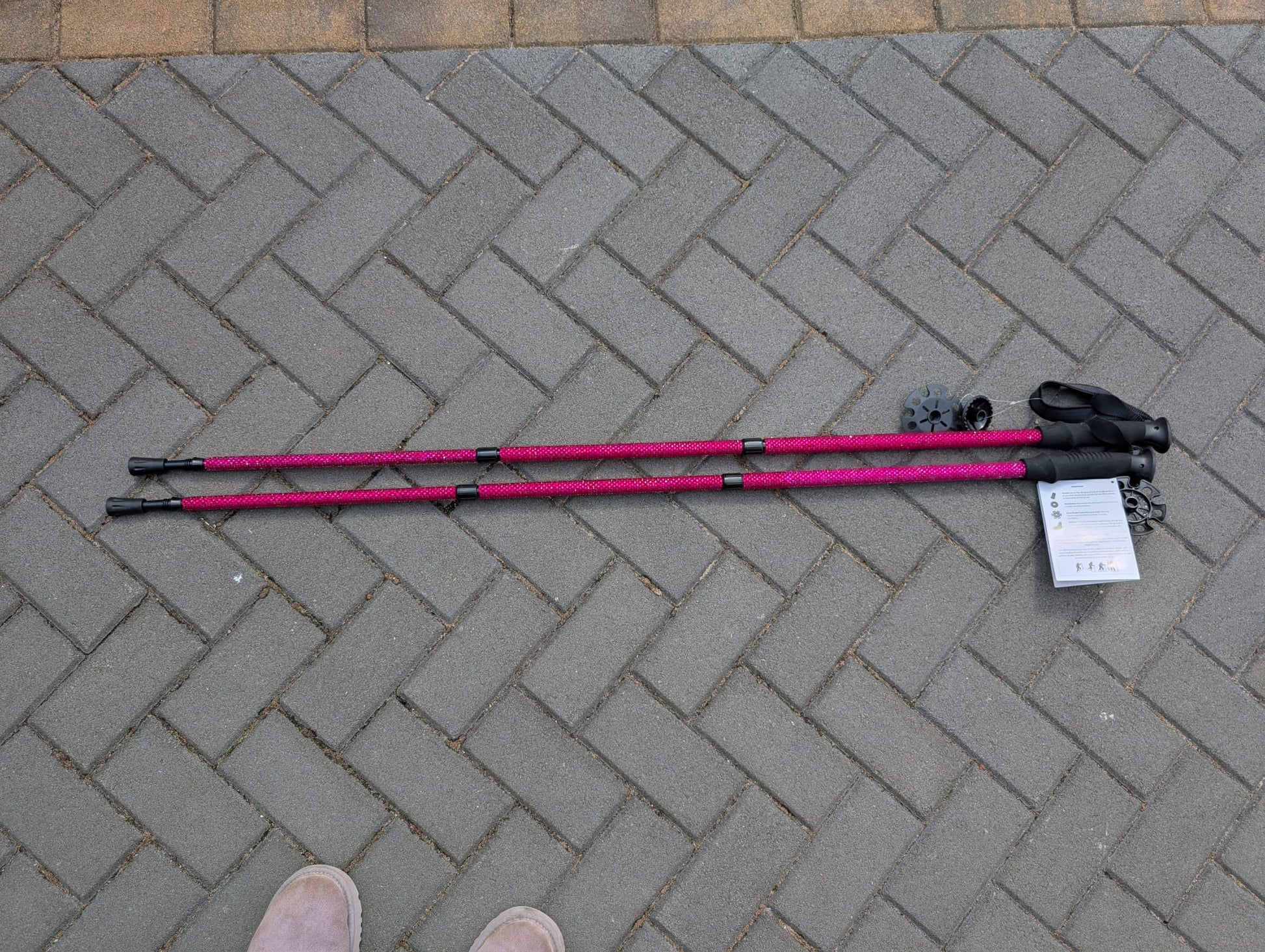Pink and black hiking poles on a grey brick pavement