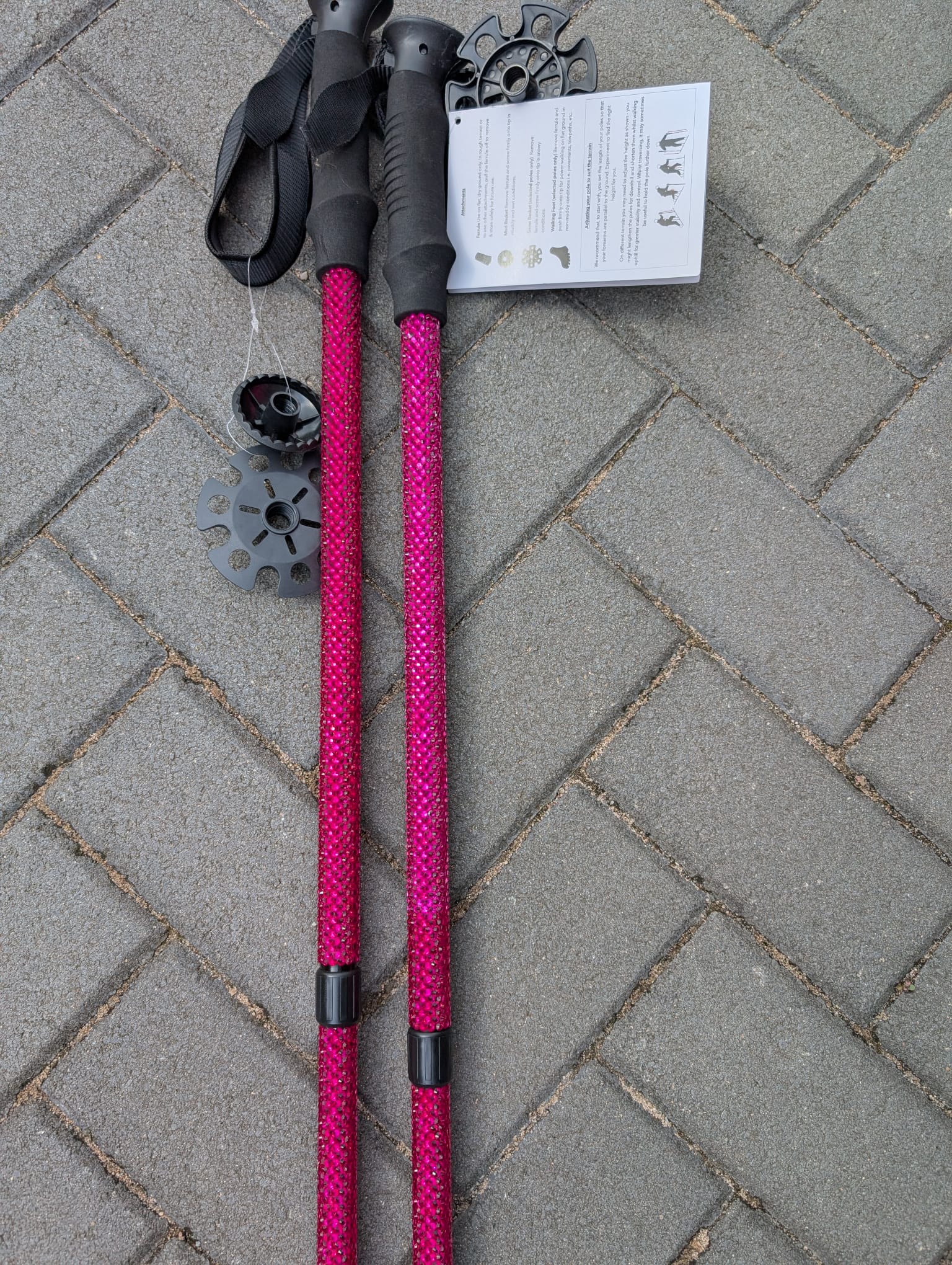 Two pink hiking poles with black grips on a grey pavement.