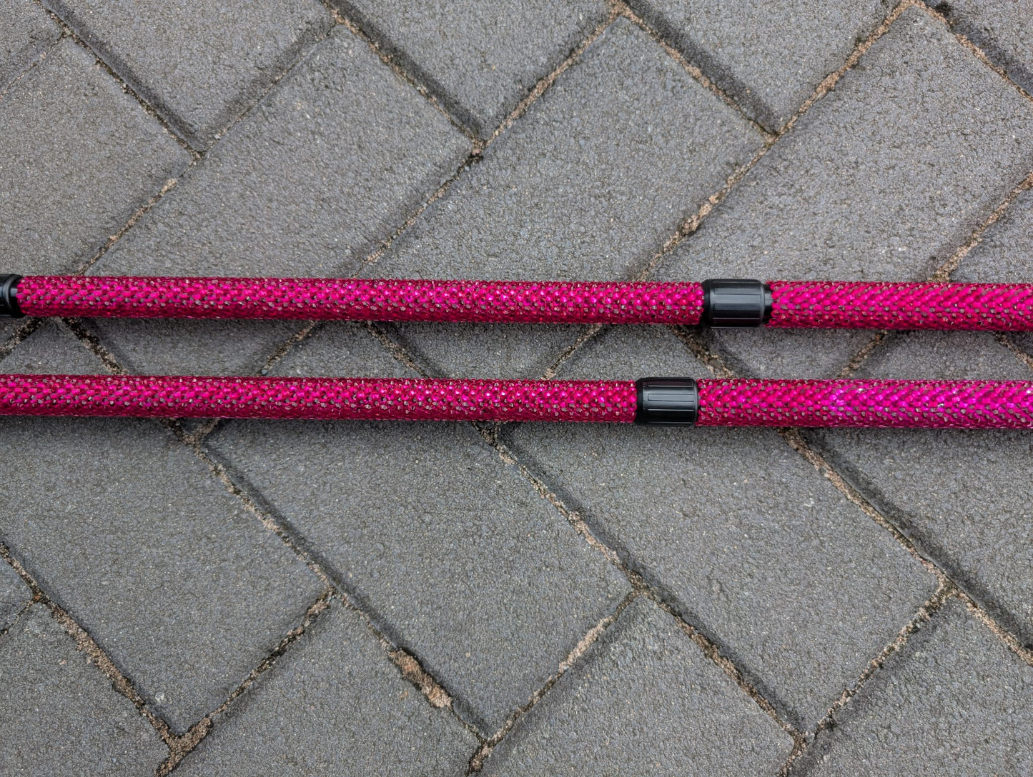 Two pink trekking poles with black ends on a gray pavement