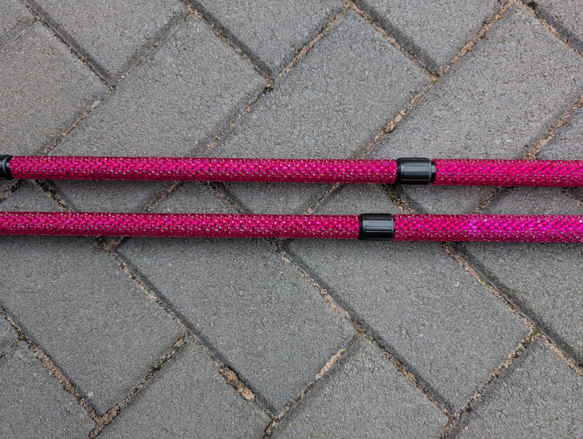 Two pink trekking poles with black ends on a gray pavement