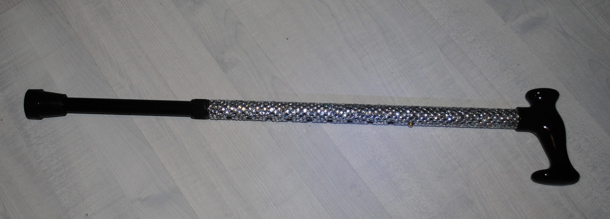 A  Sparklestick showing the shimmering Rhinestones and black handle and function to change to height. She SparkleStick is on a grey wood effect back ground