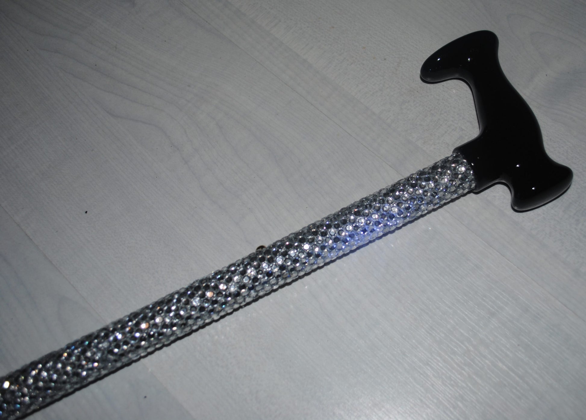 A close of up a Sparklestick showing the shimmering Rhinestones and black handle. She SparkleStick is on a grey wood effect back ground