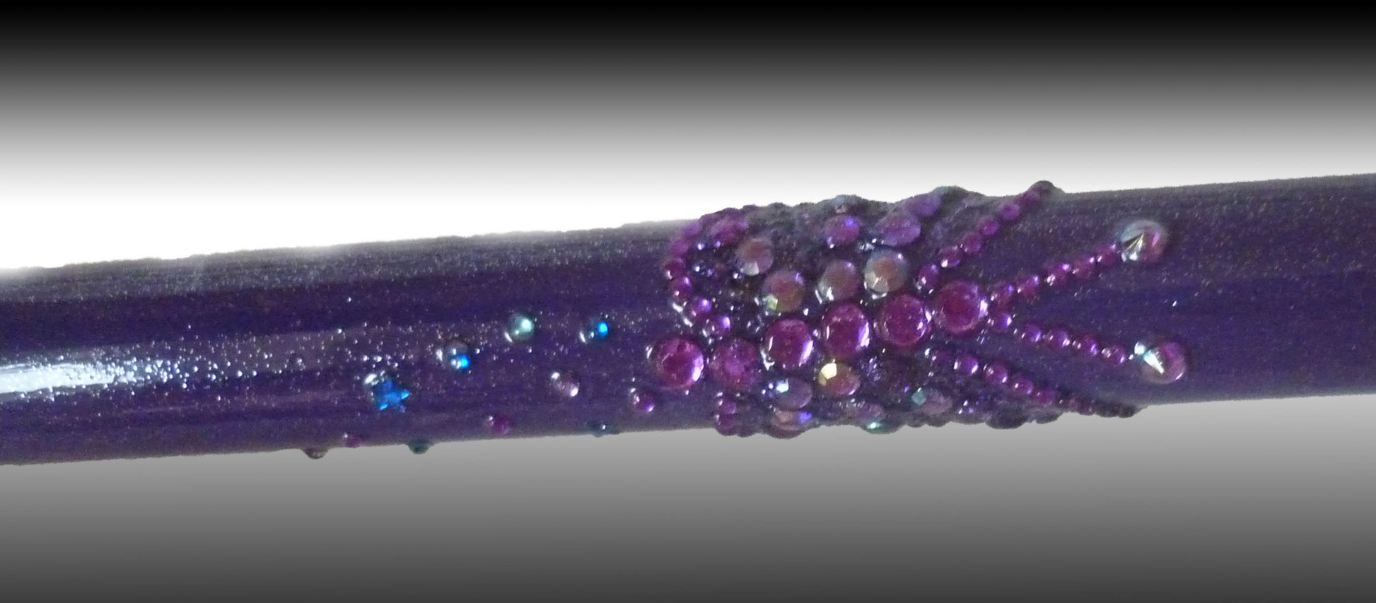 A close up of the GlitterWings folding stick which has a shimmery purple colour and is enriched with glitter butterflies picked out in purple 