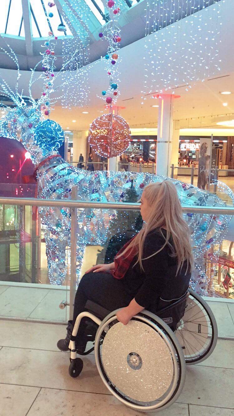 A lady in wheelchair with in shopping centre looking at the Christmas decorations